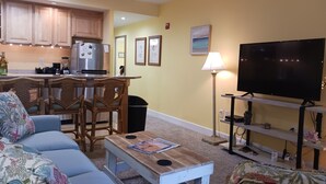 A living room with a sofa, a coffee table, a TV, and a kitchen area with cabinets and appliances.