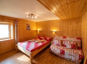 A wooden room with a bed and a sofa, both with patterned bedding. - Homerez - Apartment Gérardmer (Gérardmer)