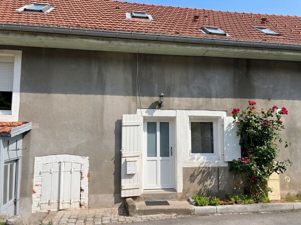 A residential building with a tiled roof, a small window with shutters, and a flower box with red flowers.