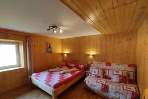 A wooden room with a bed and a sofa, both covered with patterned quilts.