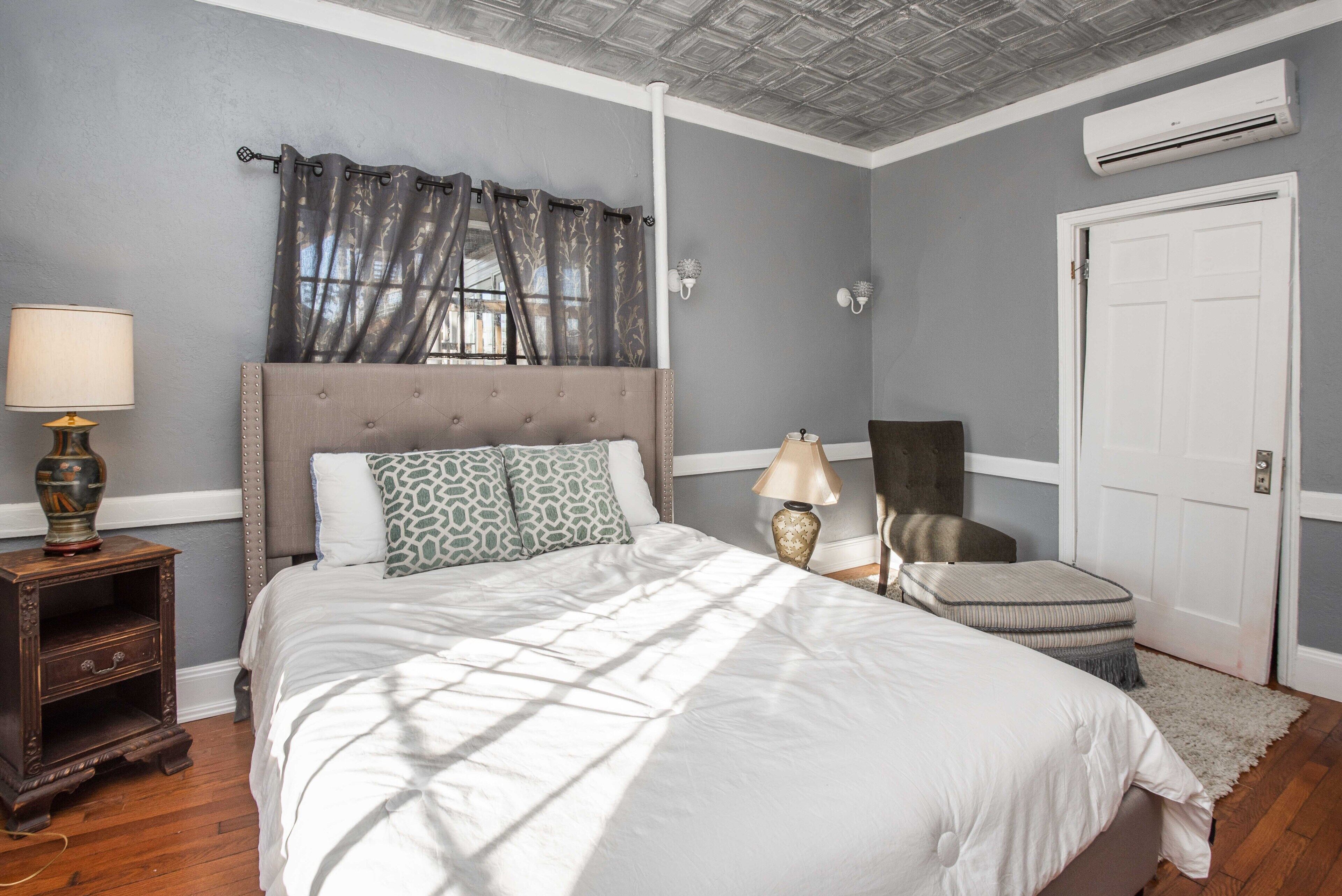 A bedroom with a large bed, a nightstand, a chair, and a door.