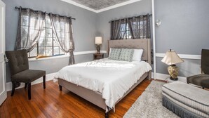 Une chambre à coucher avec un grand lit, une chaise, une table de chevet et une lampe.