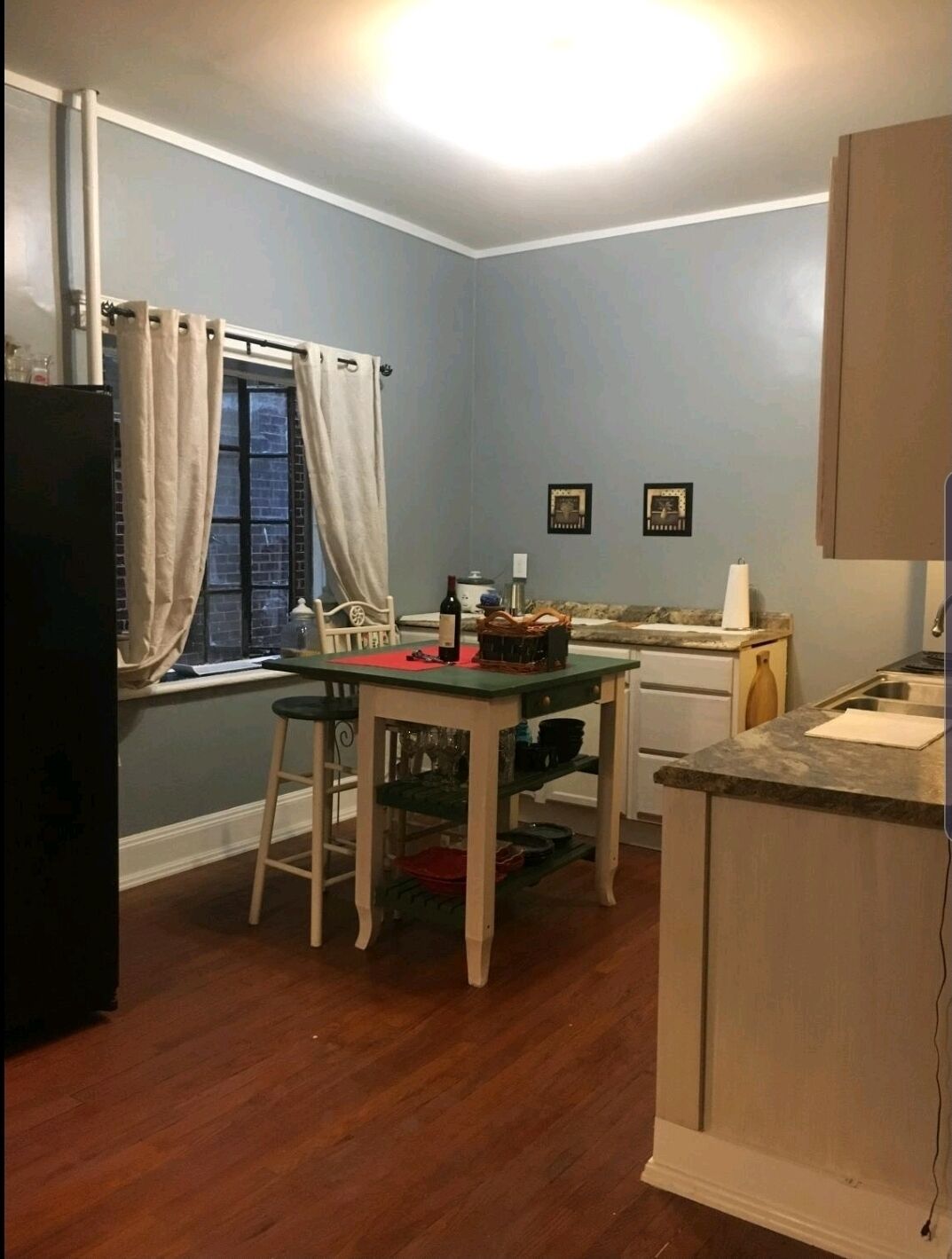 Eine kleine Küche mit Essbereich, mit einem Fenster mit Vorhängen, einem Kühlschrank und einer Spüle.