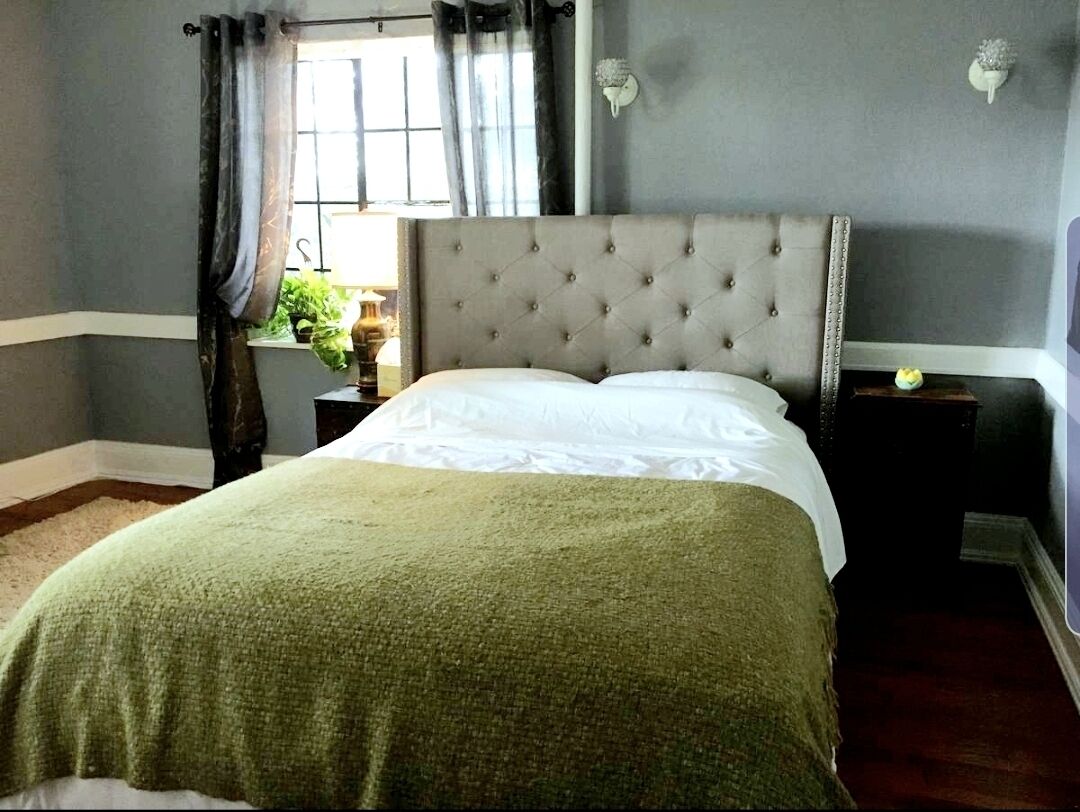 A bedroom with a tufted headboard, a green blanket, and a nightstand with a lamp.