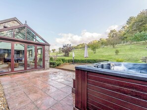 Une maison moderne dotée d’une véranda en verre, d’un jacuzzi et d’une pelouse bien entretenue.