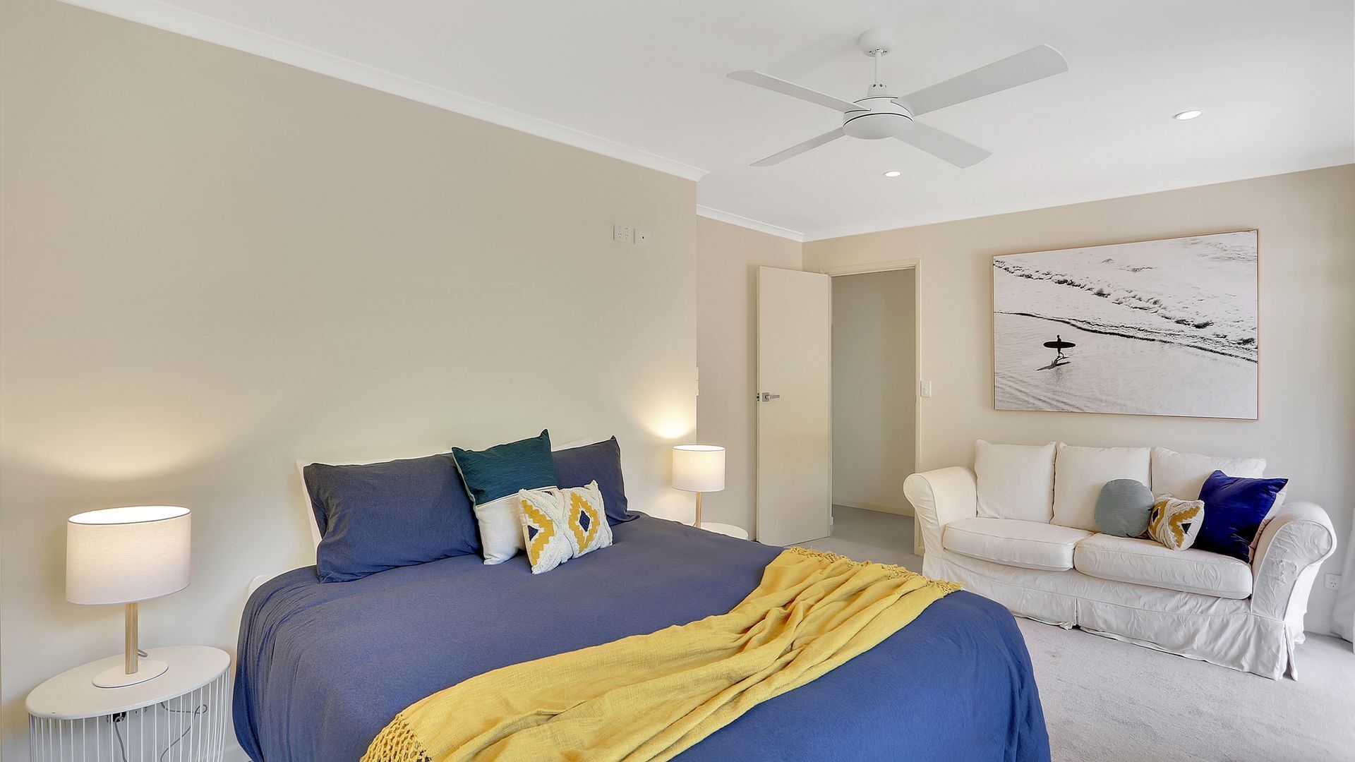 A bedroom with a bed, bedside tables, a ceiling fan, a white couch, and a wall-mounted artwork.