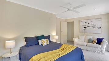 A bedroom with a bed, bedside tables, a ceiling fan, a white couch, and a wall-mounted artwork.