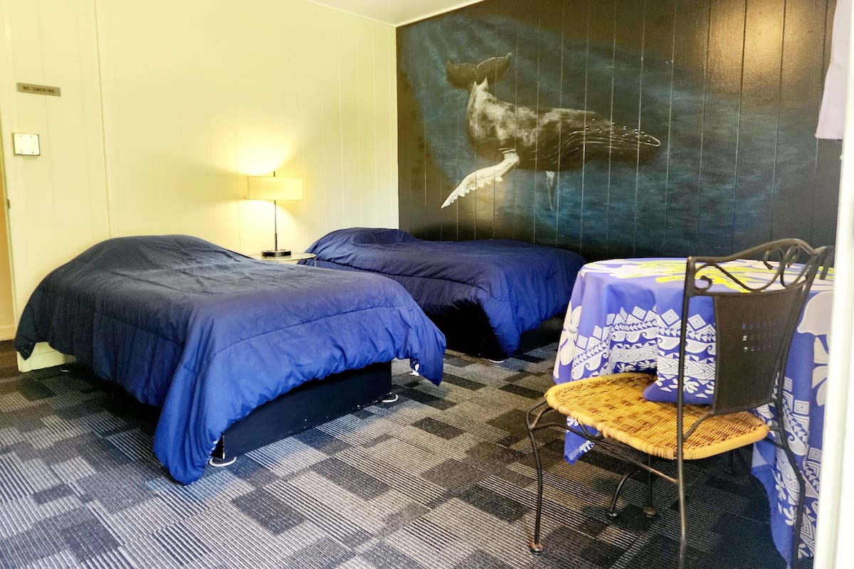 A hotel room with two beds, a table with a chair, and a wall mural.