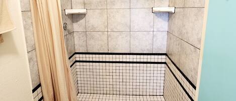 A shower with a beige curtain, tiled walls, and a black and white patterned floor.