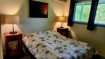 A bedroom with a bed, two bedside tables, a wall-mounted air conditioner, a window with curtains, and a painting on the wall.
