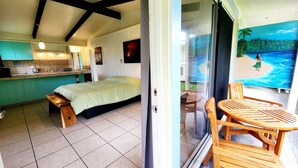 Ein Zimmer mit einem Bett, einem kleinen Tisch und Blick auf einen Strand durch eine Glastür.