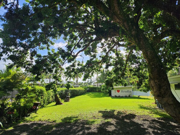 A well-maintained garden with a white RV parked in the background, surrounded by lush greenery and a clear sky. - Arnott's Lodge (Hilo)