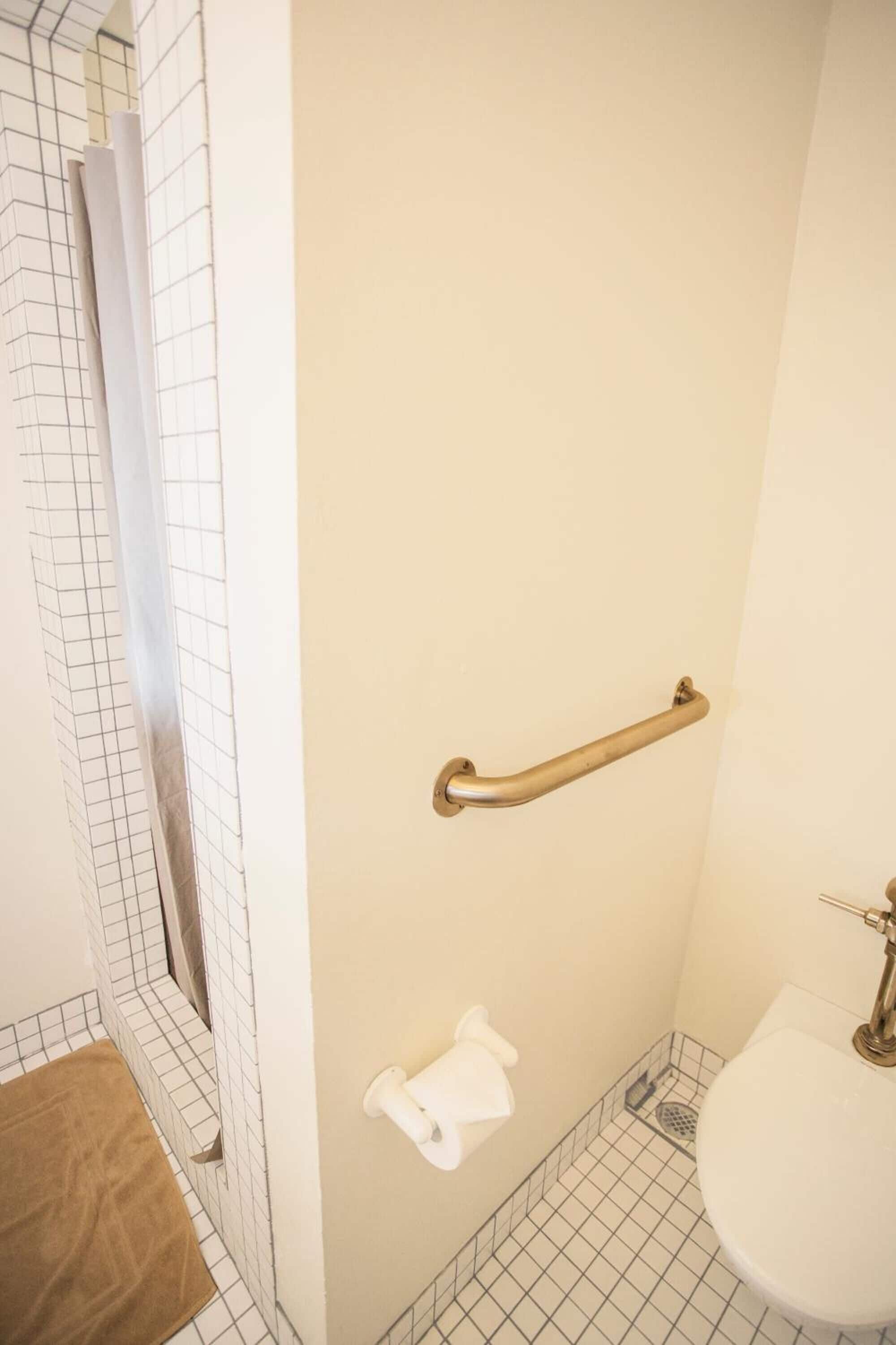 Un baño con un lavamanos blanco, un inodoro, una barra de apoyo y una zona de ducha con suelo de diseño de rejilla.