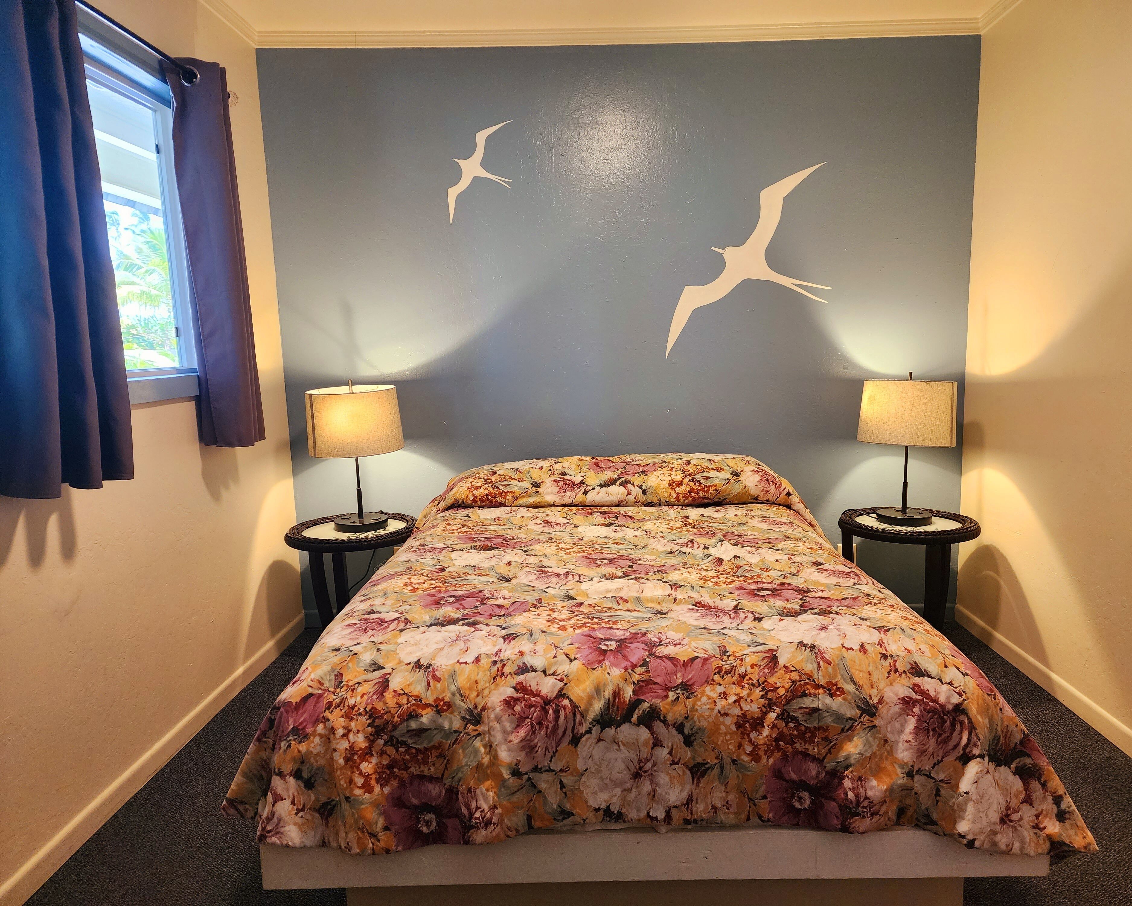A bedroom with a floral bedspread, two bedside lamps, and a wall with two bird silhouettes.