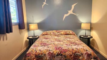 Un dormitorio con colcha de flores, dos lámparas de noche y una pared con siluetas de dos pájaros.
