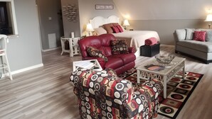 Una camera accogliente con un letto, una poltrona in pelle rossa, un poggiapiedi decorato e un divano grigio.