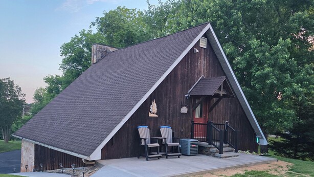 Un edificio in legno in stile cascina con tetto spiovente, un portico con sedie e una porta rossa.
