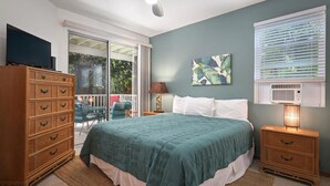 A bedroom with a bed, a dresser, a nightstand, a ceiling fan, a window with blinds, and a sliding glass door leading to an outdoor area. - Walk to Kahalu’u Beach | 2BR/2BA Condo with Lanai, Pool & A/C (Kailua-Kona)