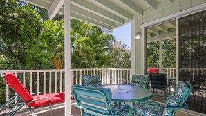 A covered patio with a round table and chairs, surrounded by lush tropical foliage. - Walk to Kahalu’u Beach | 2BR/2BA Condo with Lanai, Pool & A/C (Kailua-Kona)