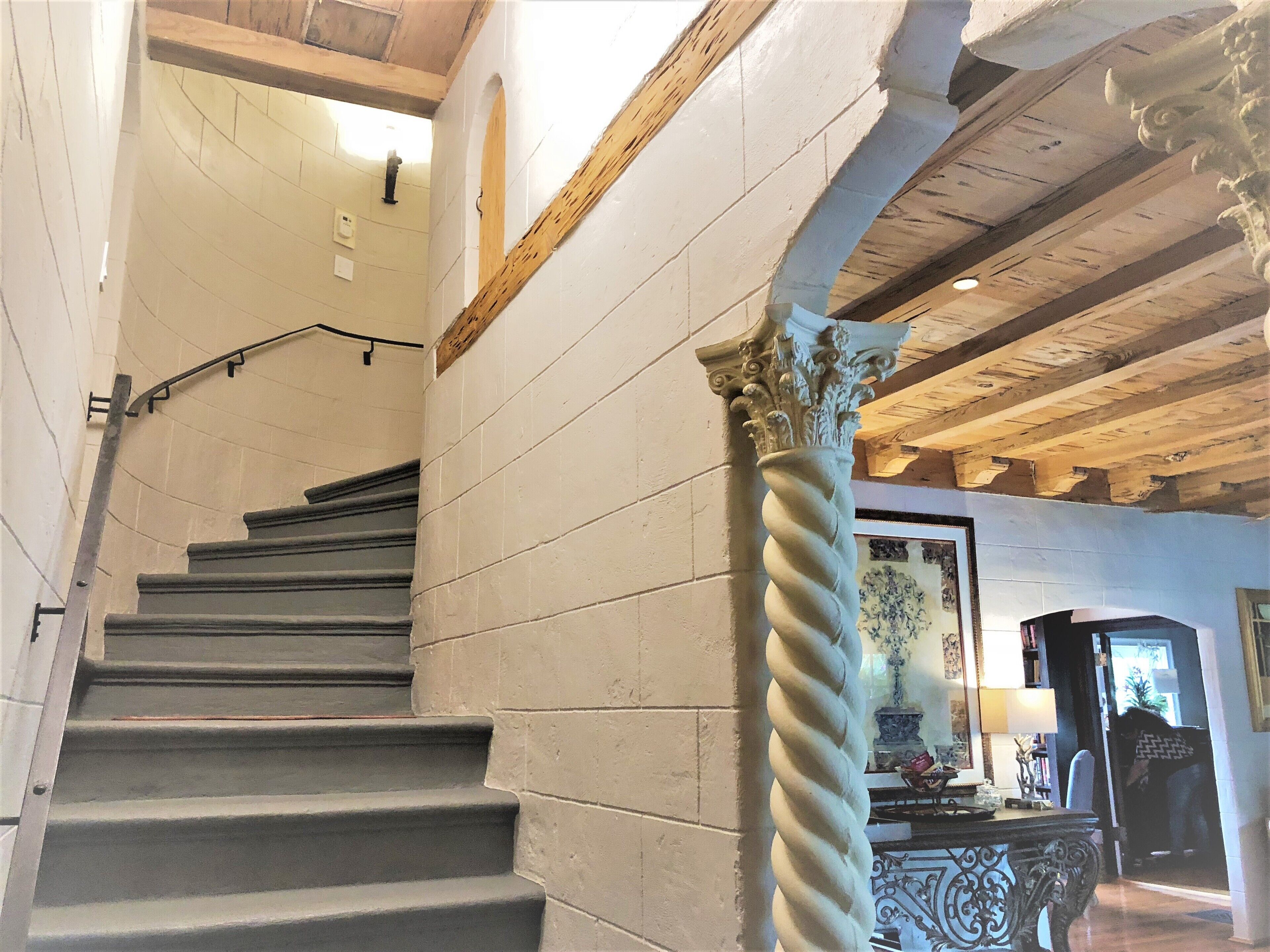 A staircase with a handrail, a decorative column, and a ceiling with exposed beams.