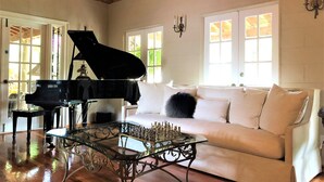 A room with a grand piano, a glass coffee table with chess pieces, a white sofa, and a wooden ceiling. - Casa Grandview Inn (West Palm Beach)