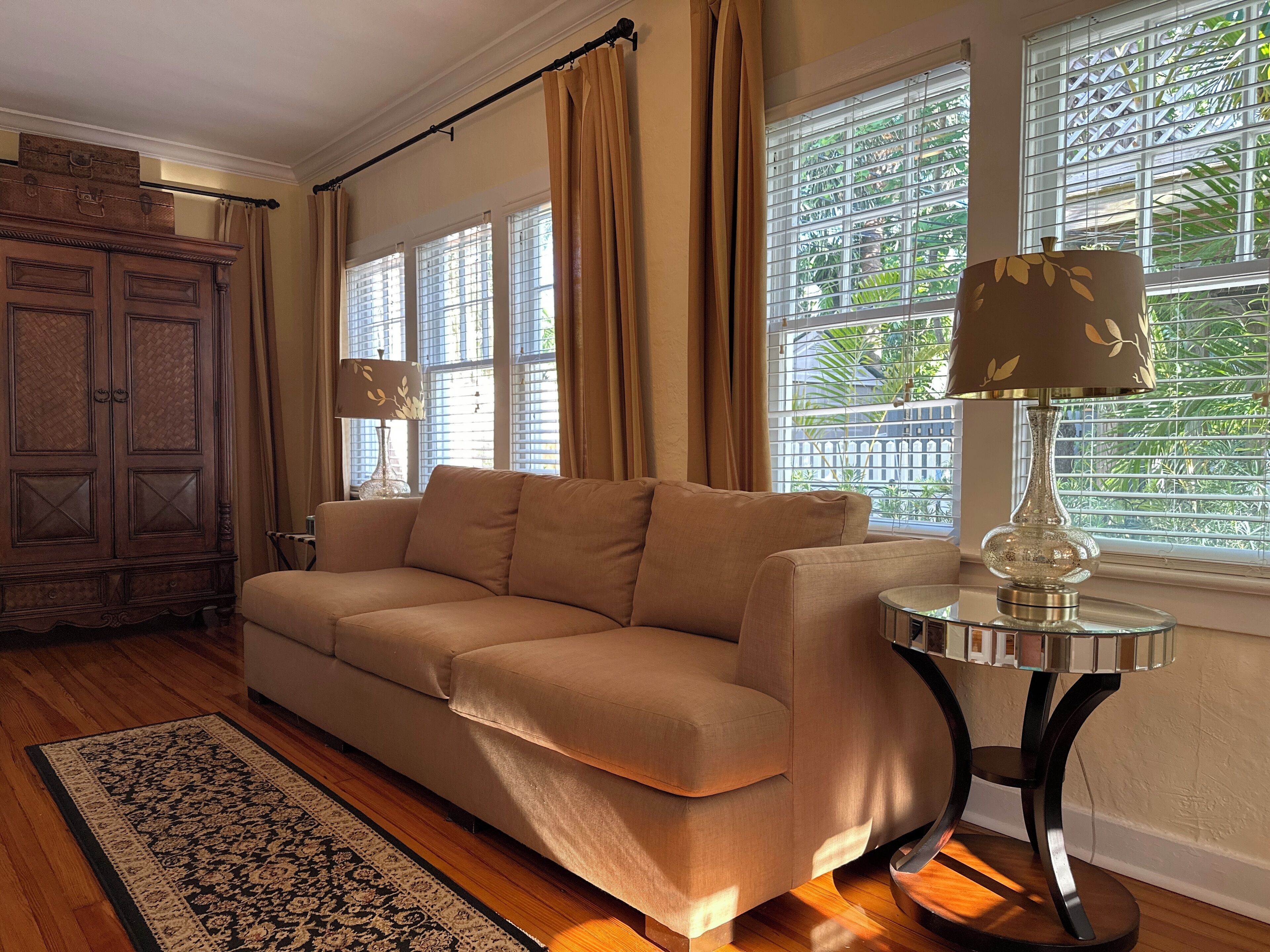 A living room with a beige sofa, a wooden cabinet, a patterned rug, and a table with a lamp.