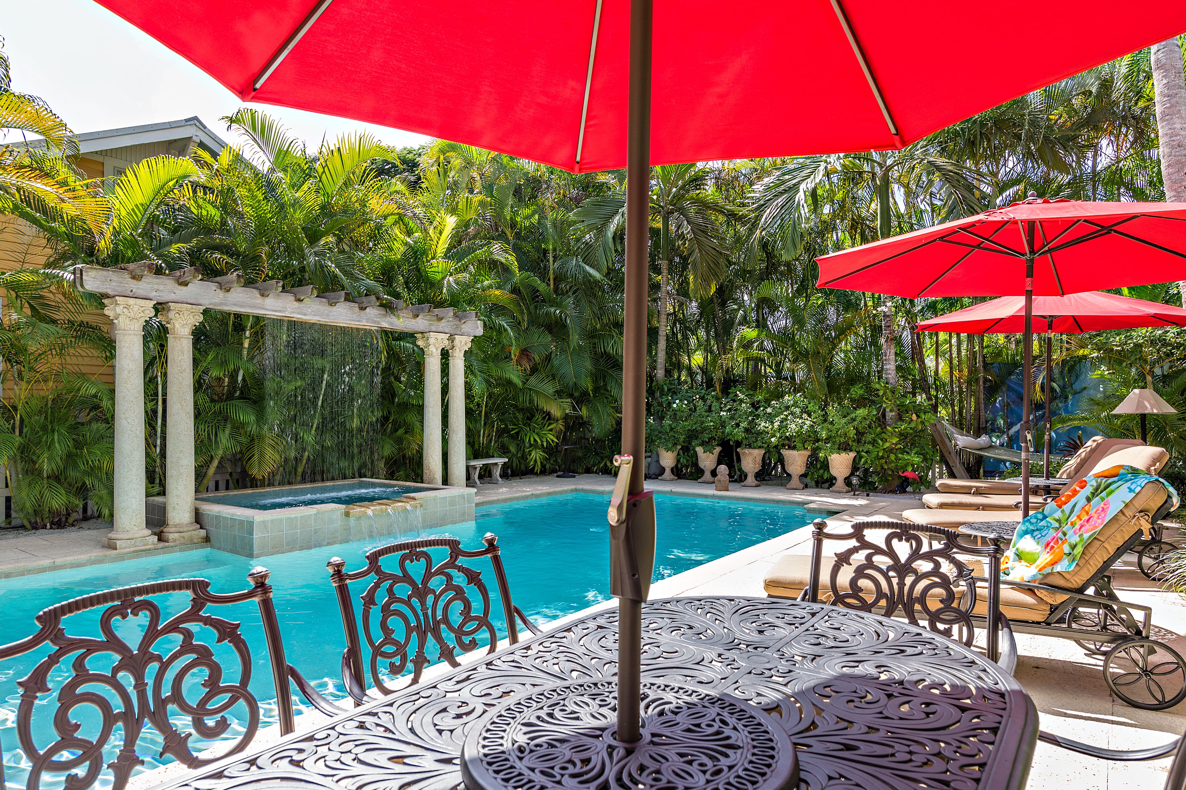 A pool area with a pergola, lounge chairs, and a table with an umbrella.