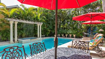 A pool area with a pergola, lounge chairs, and a table with an umbrella.