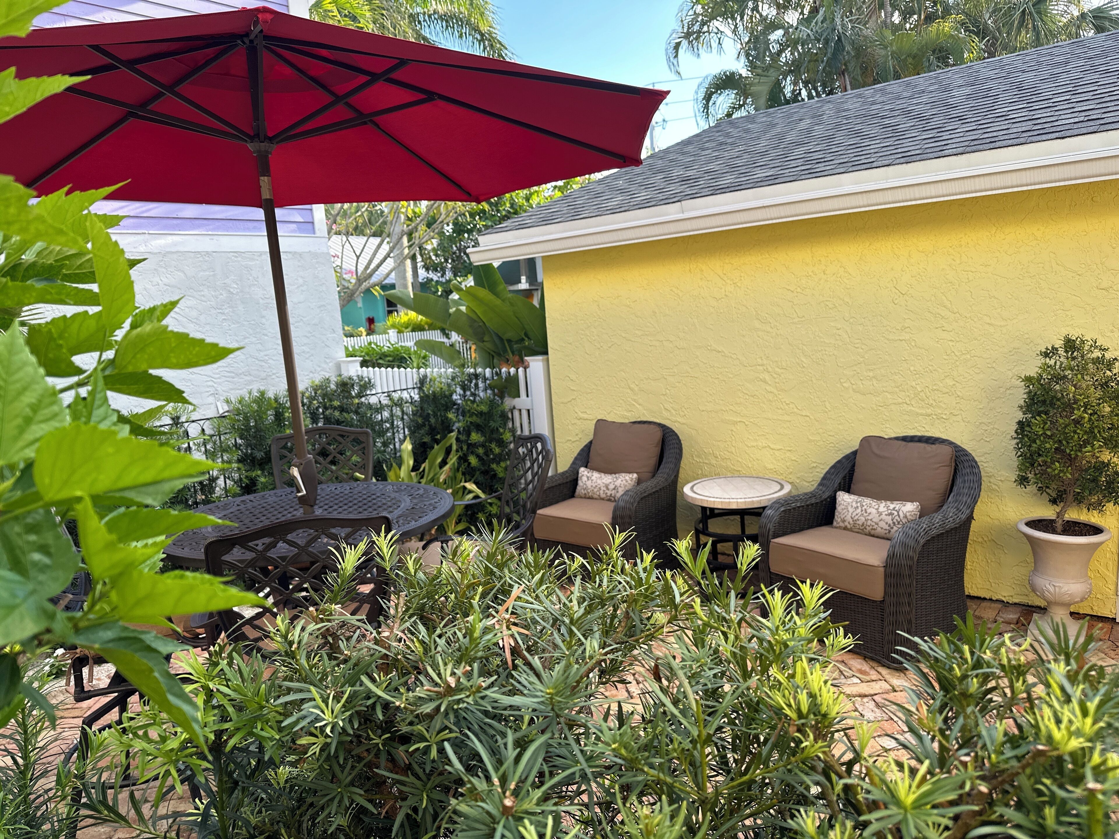 A patio area with wicker furniture, a red umbrella, and potted plants.