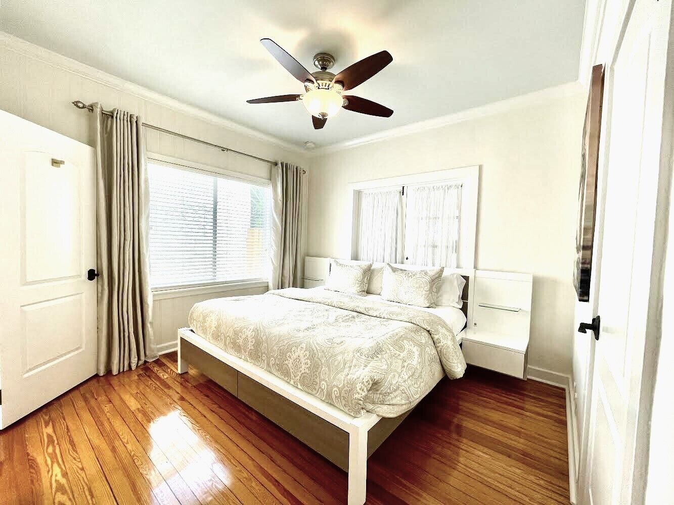 A bedroom with a bed, a ceiling fan, and a window with curtains.