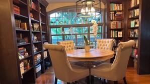 A library with a round wooden table and four chairs, surrounded by tall bookshelves filled with books. - Casa Grandview Inn (West Palm Beach)