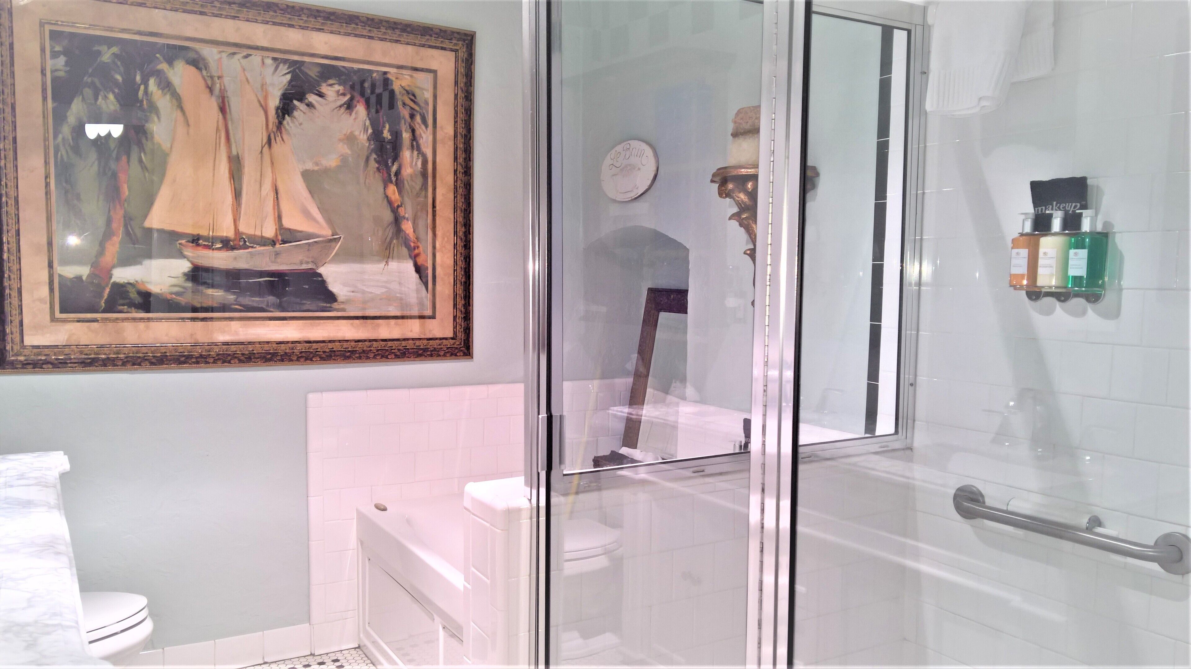 A bathroom with a glass shower enclosure, a toilet, a sink, and a framed painting on the wall.
