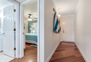 Un pasillo con suelo de madera, una puerta blanca y una cama con una colcha azul al fondo.
