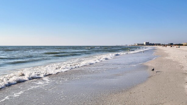Ein Strand mit blauem Himmel, Wellen und Gebäuden in der Ferne.