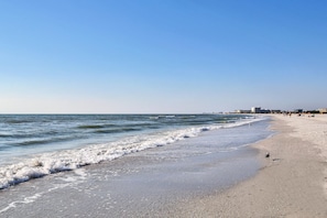 Ein Strand mit blauem Himmel, Wellen und Gebäuden in der Ferne.