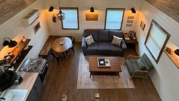 A loft-style room with a sloped ceiling, a ceiling fan, a sofa, a coffee table, a dining table, and a kitchen area. - Black Hills Farmhouse, Guest House #1 (Custer)
