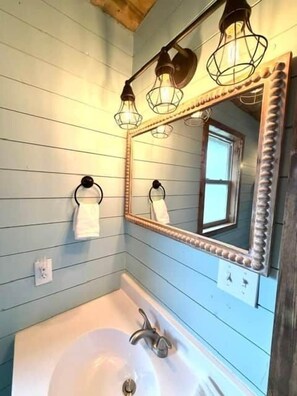 A bathroom with a large mirror, a sink, and hanging light fixtures. - Black Hills Farmhouse, Guest House #1 (Custer)
