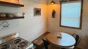 A kitchen with a stove, a dining table with chairs, a hanging light fixture, and a window with blinds. - Black Hills Farmhouse, Guest House #1 (Custer)