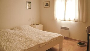 Ett sovrum med en säng, ett sängbord, en lampa, ett element och ett fönster med gardiner.