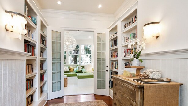A hallway with bookshelves, a wooden dresser, and a window with a view of greenery. - Elegant Coastal Escape | Steps to the Beach (Tybee Island)