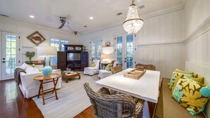 A spacious living room with a white sofa, a dining table, wicker chairs, and a chandelier. - Elegant Coastal Escape | Steps to the Beach (Tybee Island)
