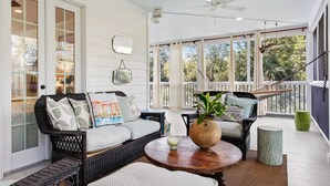 A covered porch with wicker furniture, a ceiling fan, and large windows offering views of the outdoors. - Elegant Coastal Escape | Steps to the Beach (Tybee Island)