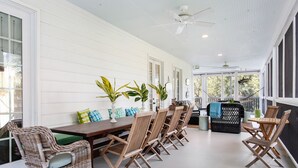 A covered patio with a dining area, wicker chairs, and a black sofa. - Elegant Coastal Escape | Steps to the Beach (Tybee Island)