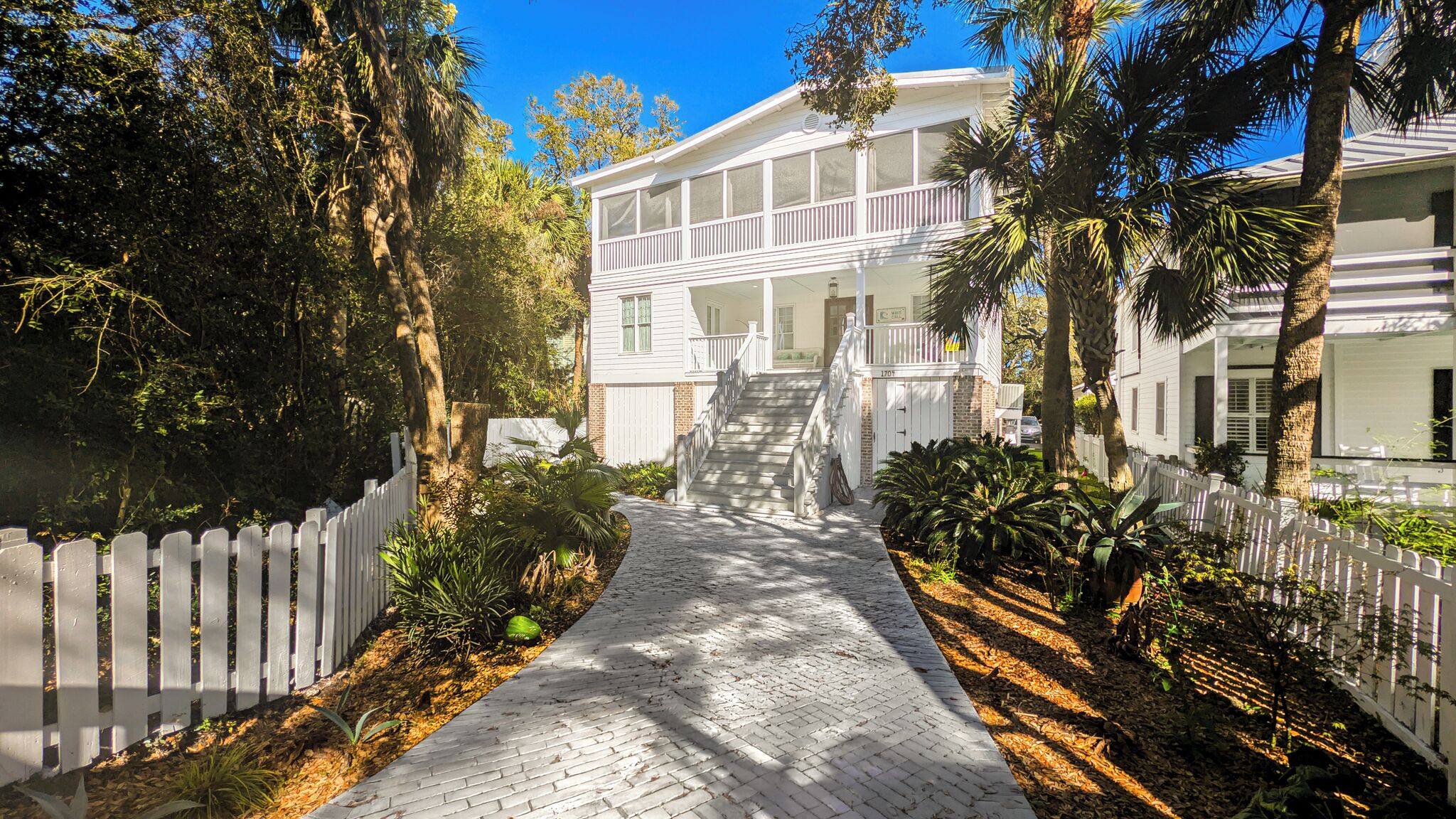 A pathway leading to a white building with a porch and a staircase.