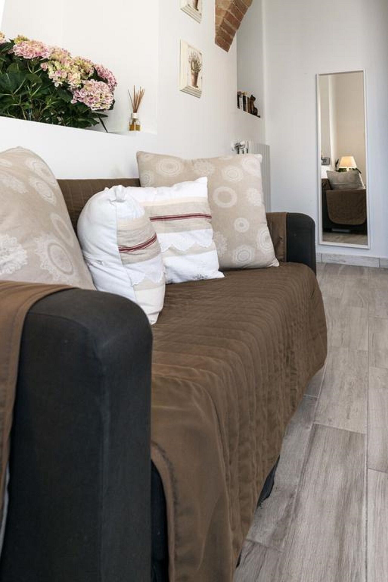 Una sala moderna con un sofá marrón, cojines estampados y un jarrón de flores sobre una pared blanca.