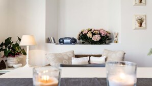 Uma sala de estar aconchegante com um sofá, uma luminária, um rádio e um vaso de flores.