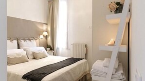 Quarto com cama, mesa de cabeceira, luminária e espelho com porta-toalhas.