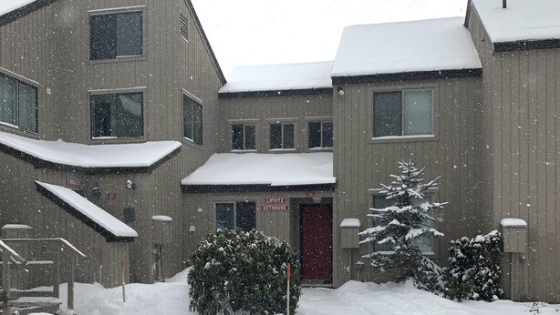 Ein Gebäude mit mehreren Fenstern und einer roten Tür, umgeben von schneebedecktem Boden und Bäumen.