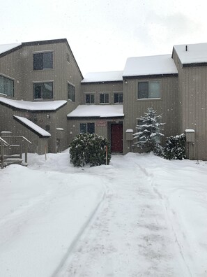 Un edificio con múltiples ventanas y una puerta roja, rodeado de nieve y árboles.