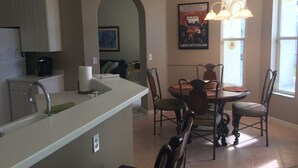 Une cuisine moderne dotée d’un îlot central, d’une table à manger et de chaises. Un poster orne le mur et une fenêtre laisse entrer la lumière naturelle.